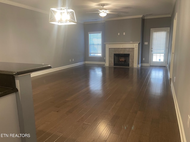 unfurnished living room featuring a healthy amount of sunlight, dark wood-style floors, a tile fireplace, and ornamental molding