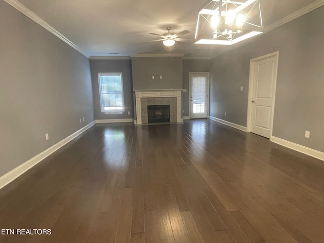 unfurnished living room featuring baseboards, dark wood finished floors, a tiled fireplace, crown molding, and ceiling fan with notable chandelier