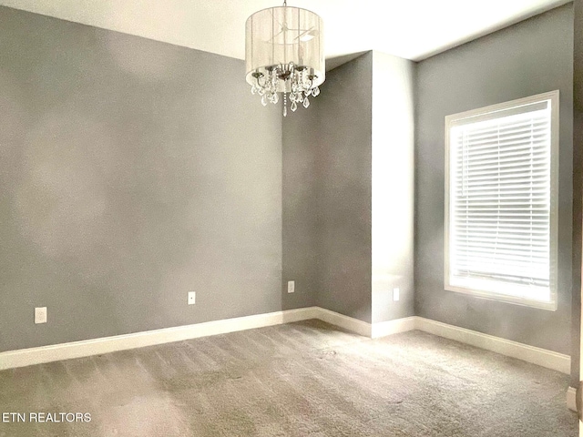 unfurnished room with baseboards, a chandelier, and carpet flooring