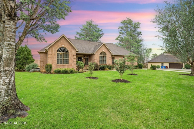 ranch-style house featuring a garage, a yard, roof with shingles, and brick siding