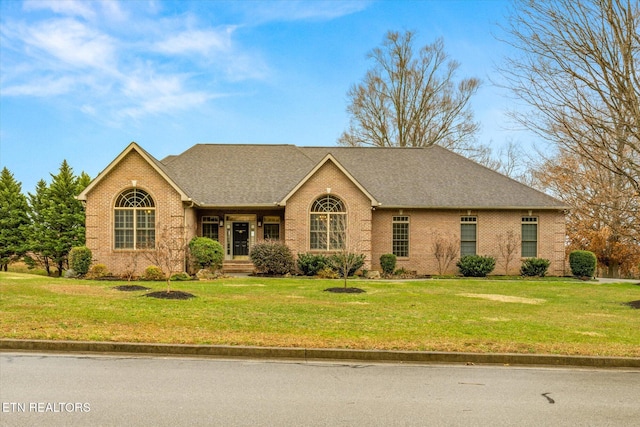 ranch-style house with brick siding, a front lawn, and roof with shingles