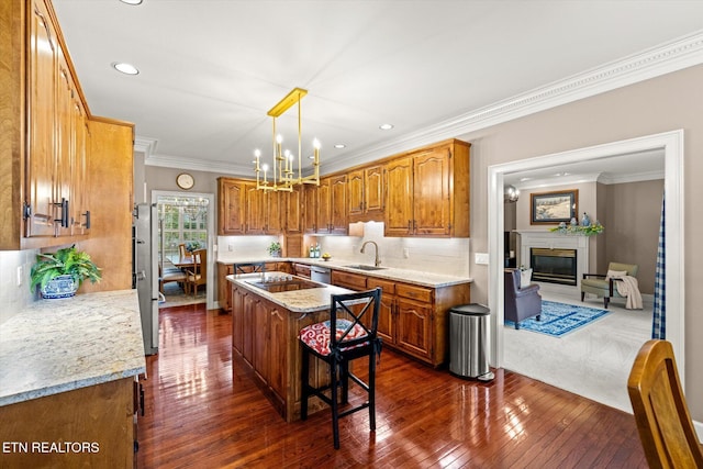 kitchen featuring a glass covered fireplace, a kitchen island, brown cabinets, a chandelier, and a sink