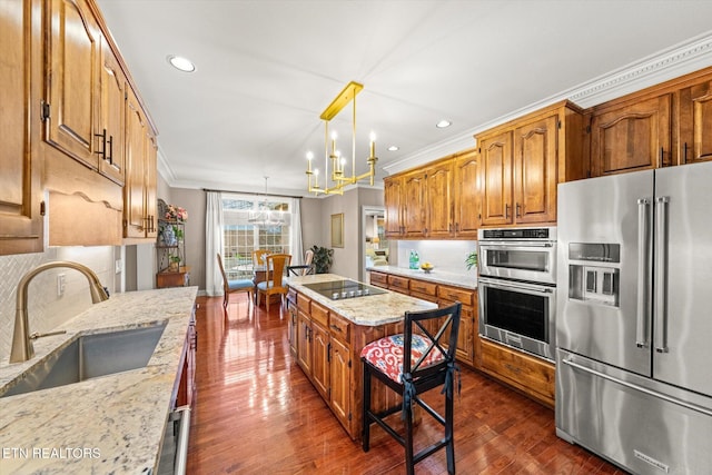 kitchen with a notable chandelier, a sink, appliances with stainless steel finishes, brown cabinetry, and crown molding