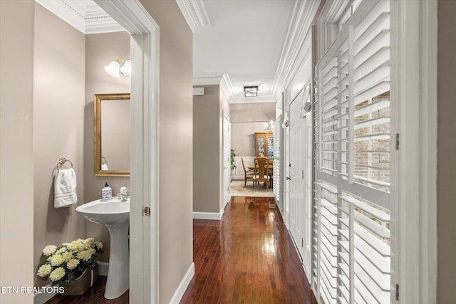 corridor featuring baseboards, a sink, hardwood / wood-style flooring, and crown molding