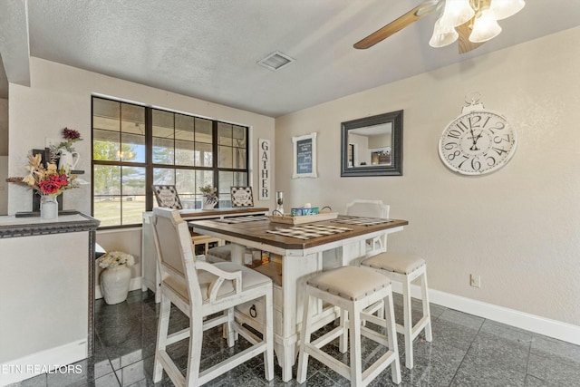 dining space with a textured ceiling, ceiling fan, granite finish floor, visible vents, and baseboards