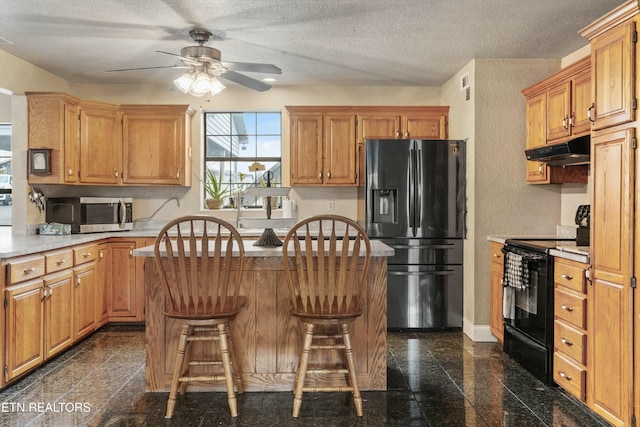 kitchen featuring baseboards, a kitchen island, under cabinet range hood, black appliances, and granite finish floor