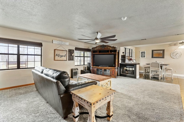 carpeted living room with a fireplace, ceiling fan, a textured ceiling, and baseboards