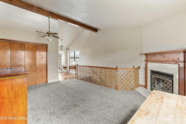 carpeted living area with vaulted ceiling with beams, a fireplace with flush hearth, a ceiling fan, and baseboards