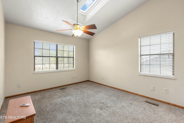 unfurnished room featuring lofted ceiling with skylight, a ceiling fan, visible vents, and carpet flooring