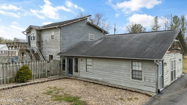 back of house featuring fence and roof with shingles