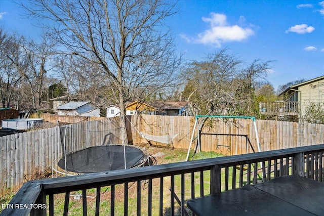 deck featuring a fenced backyard, a lawn, and a trampoline