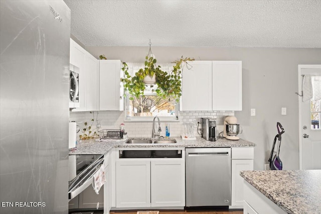 kitchen featuring tasteful backsplash, light stone countertops, appliances with stainless steel finishes, white cabinets, and a sink