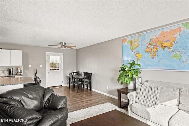living room with ceiling fan, baseboards, dark wood-style flooring, and a textured ceiling