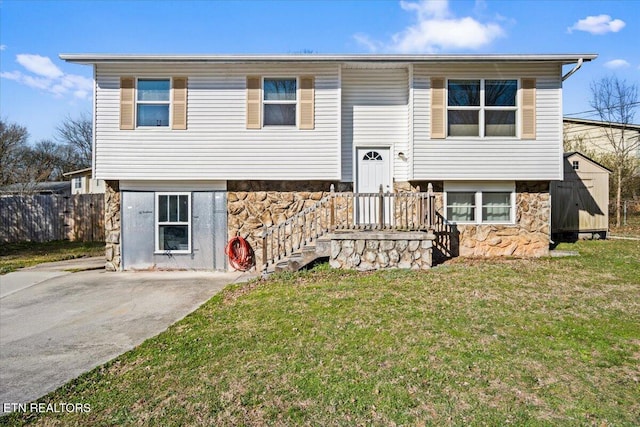 raised ranch with fence, a shed, a front lawn, an outdoor structure, and stone siding