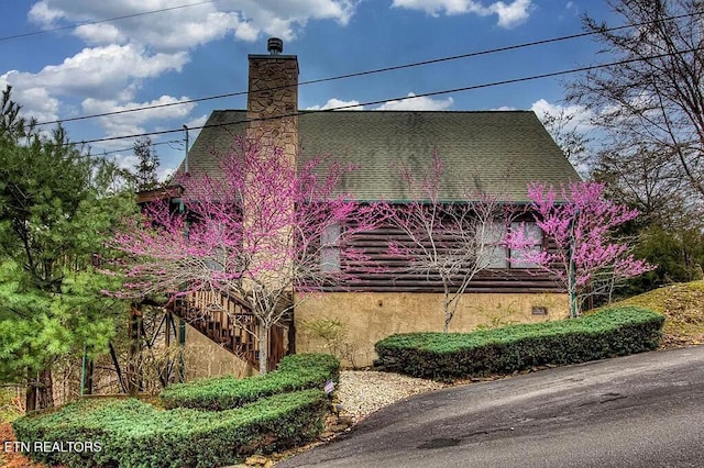 view of home's exterior featuring a shingled roof, stairs, a chimney, and stucco siding