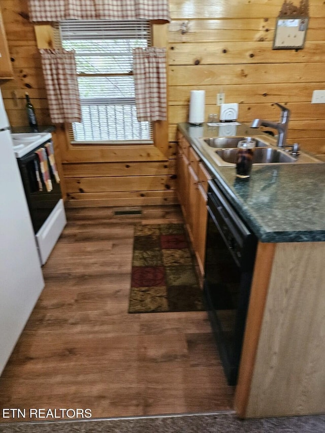 kitchen with dark wood finished floors, dark countertops, a sink, wooden walls, and dishwasher