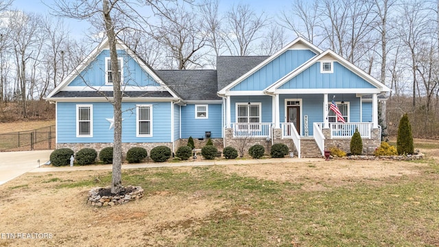 view of front of property with covered porch, fence, roof with shingles, board and batten siding, and a front yard