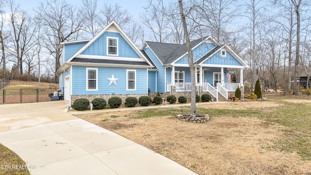 craftsman-style house featuring covered porch, a shingled roof, driveway, board and batten siding, and a front yard