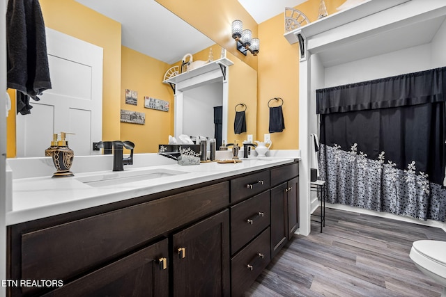 full bath with curtained shower, toilet, wood finished floors, a sink, and double vanity