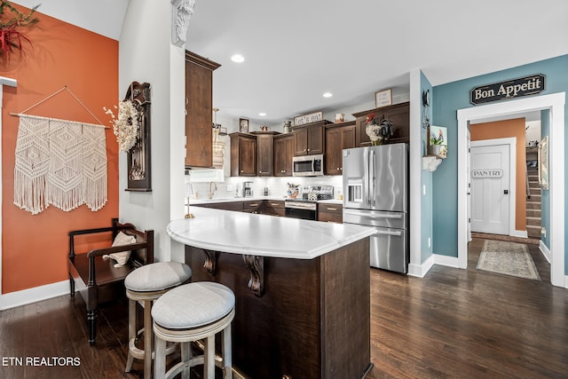 kitchen with a peninsula, dark brown cabinets, appliances with stainless steel finishes, light countertops, and dark wood-style floors