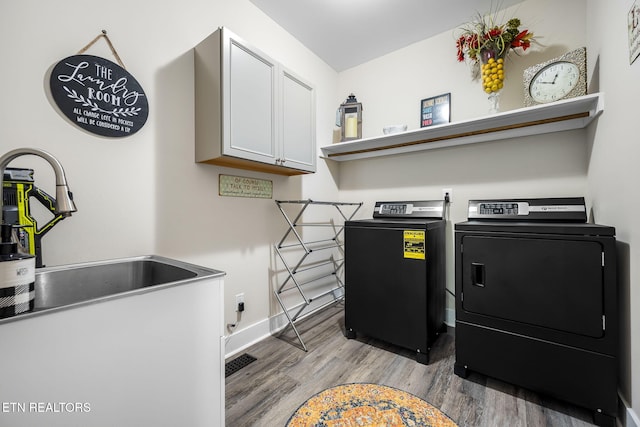 washroom with washer and clothes dryer, cabinet space, a sink, light wood-type flooring, and baseboards