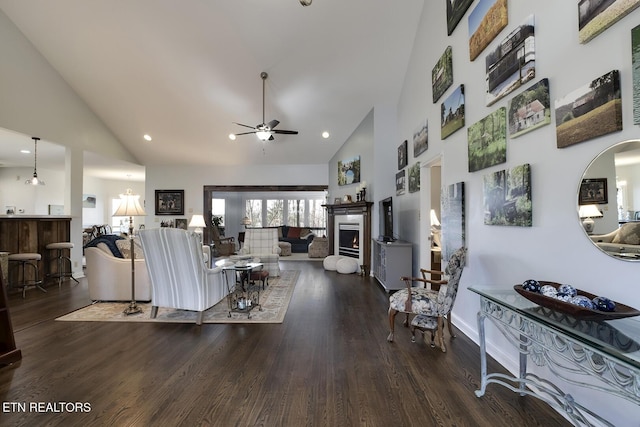 living area with a warm lit fireplace, high vaulted ceiling, ceiling fan, and wood finished floors