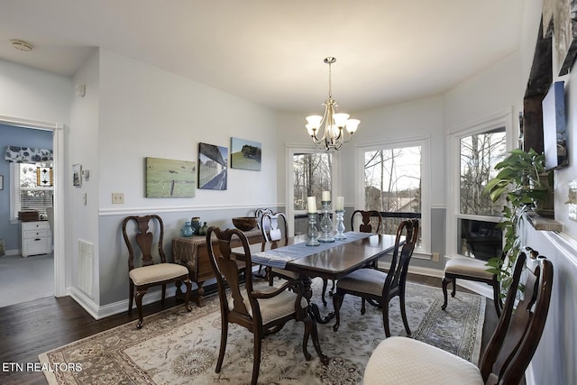 dining space featuring baseboards, visible vents, a notable chandelier, and wood finished floors