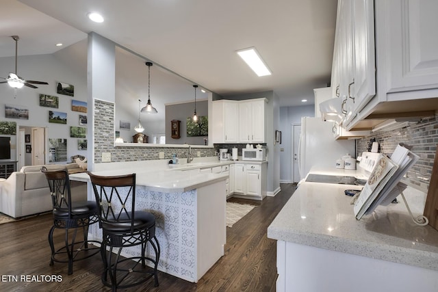 kitchen with a peninsula, a breakfast bar, dark wood-style flooring, a sink, and hanging light fixtures