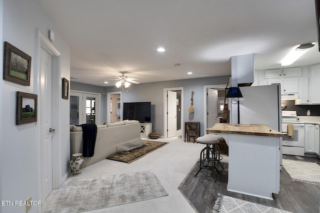 kitchen featuring white electric stove, white cabinets, wood counters, a kitchen breakfast bar, and under cabinet range hood