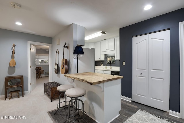 kitchen with butcher block counters, freestanding refrigerator, white cabinets, a sink, and a kitchen breakfast bar