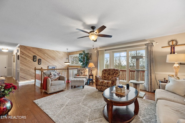 living room featuring wooden walls, a ceiling fan, hardwood / wood-style flooring, crown molding, and a textured ceiling