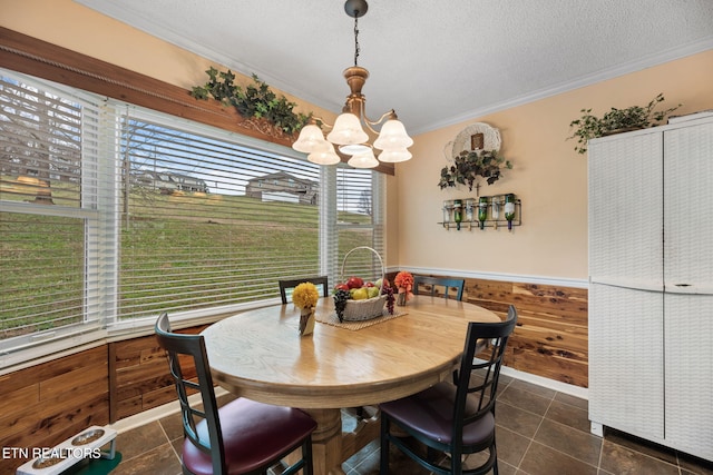 dining space featuring wooden walls, a wainscoted wall, an inviting chandelier, a textured ceiling, and crown molding