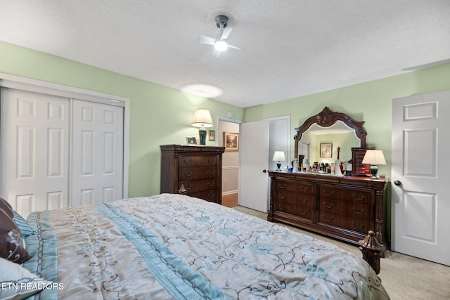 bedroom featuring a textured ceiling, ceiling fan, a closet, and light colored carpet