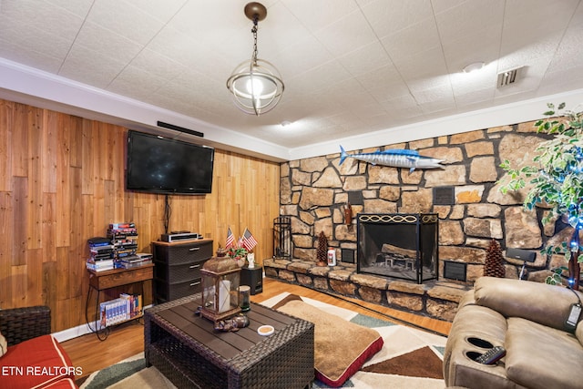 living area featuring wood walls, visible vents, wood finished floors, and a stone fireplace