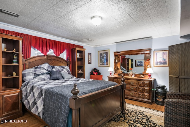 bedroom featuring visible vents, ornamental molding, and wood finished floors