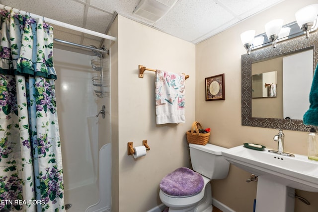 full bathroom with baseboards, a shower with shower curtain, toilet, a paneled ceiling, and a sink