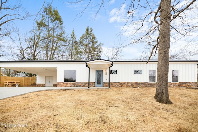 mid-century home with a carport, stone siding, fence, and concrete driveway