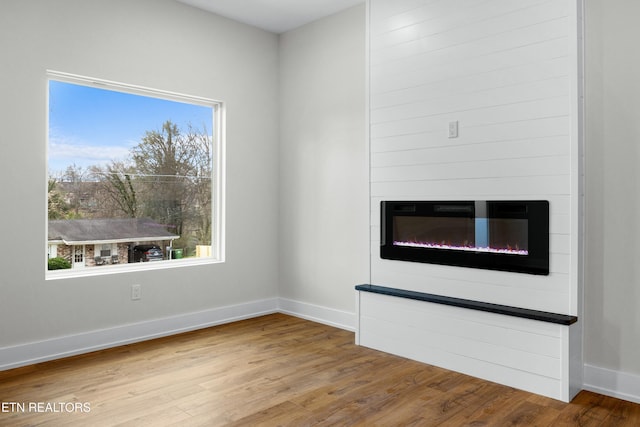 unfurnished living room with wood finished floors, plenty of natural light, a glass covered fireplace, and baseboards