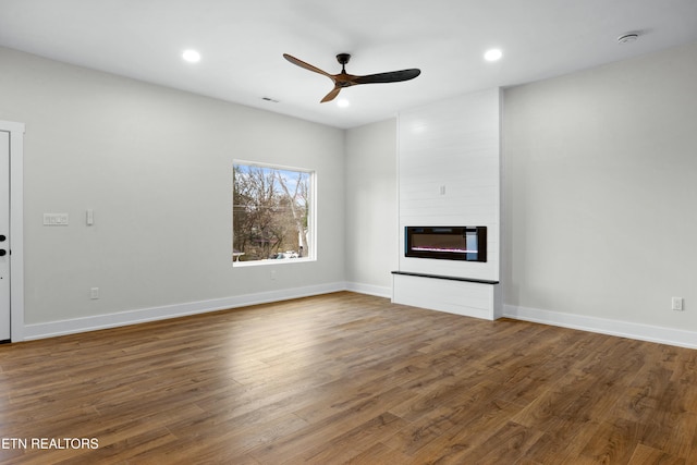 unfurnished living room with ceiling fan, recessed lighting, a large fireplace, wood finished floors, and baseboards