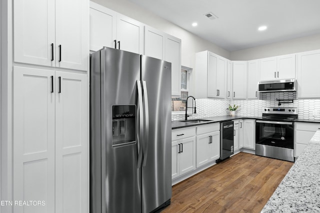 kitchen with tasteful backsplash, white cabinets, appliances with stainless steel finishes, dark wood-style flooring, and a sink