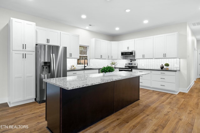 kitchen featuring a center island, stainless steel appliances, white cabinetry, a sink, and wood finished floors