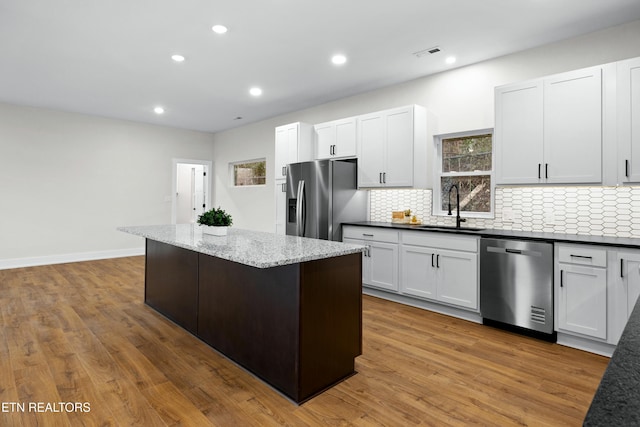 kitchen with stainless steel appliances, a kitchen island, a sink, visible vents, and backsplash