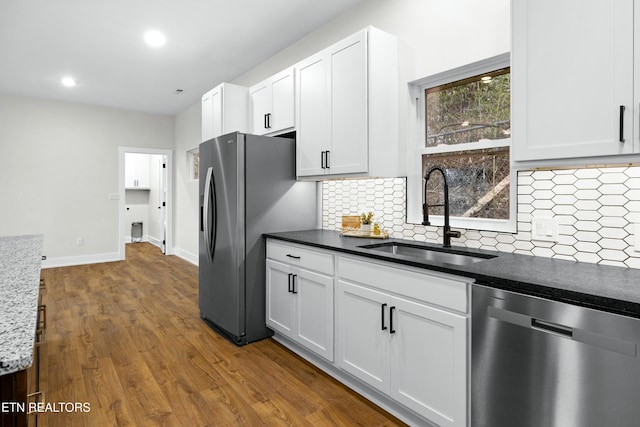 kitchen with white cabinets, decorative backsplash, dark wood-style floors, appliances with stainless steel finishes, and a sink