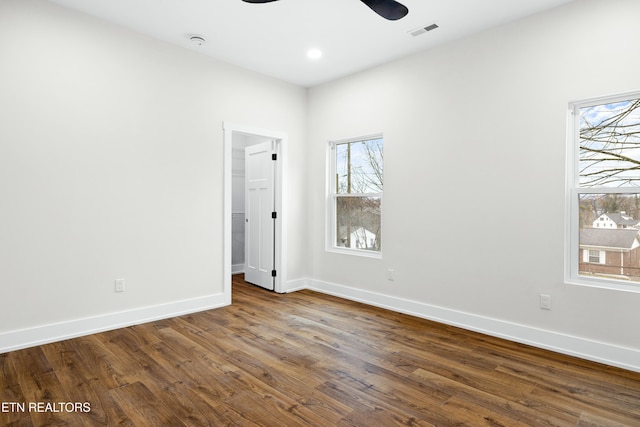 empty room featuring dark wood-style floors, baseboards, visible vents, and a ceiling fan