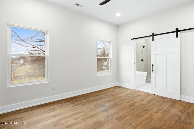 empty room featuring a barn door, baseboards, visible vents, ceiling fan, and wood finished floors