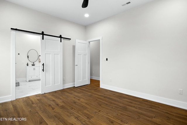 unfurnished bedroom with visible vents, ensuite bathroom, a barn door, wood finished floors, and baseboards