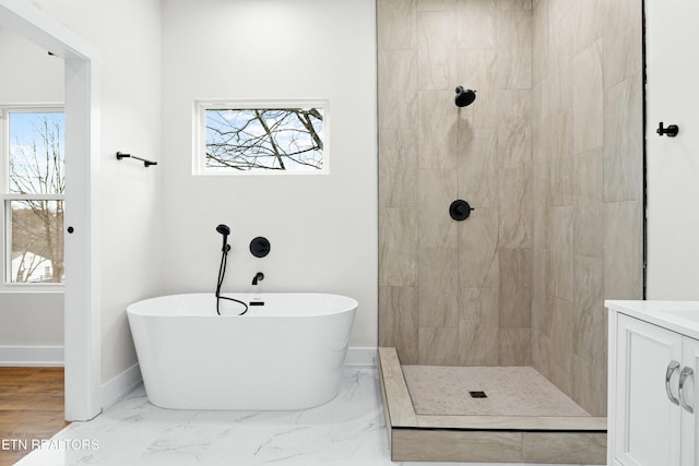 bathroom featuring marble finish floor, a soaking tub, a tile shower, vanity, and baseboards