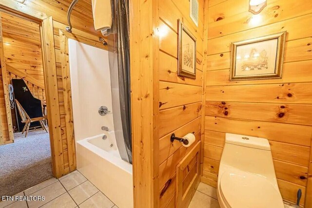 full bath with tile patterned flooring, wooden walls, toilet, and shower / bathtub combination