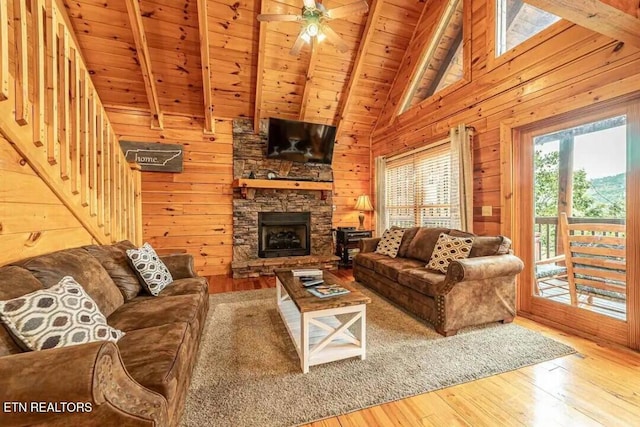 living room with beam ceiling, wooden walls, a stone fireplace, wooden ceiling, and hardwood / wood-style floors