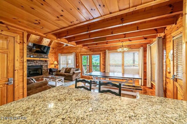 kitchen with a stone fireplace, wood walls, wooden ceiling, and light stone countertops